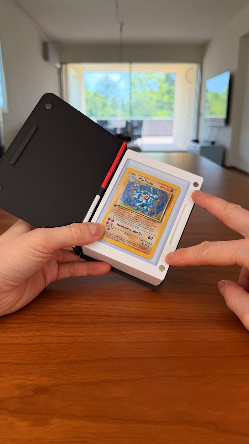 Puede incluir: Un estuche de exhibici&oacute;n magn&eacute;tico en blanco y negro que contiene una carta coleccionable de Machamp. El estuche tiene una cubierta negra y un marco blanco con cuatro peque&ntilde;os imanes circulares en las esquinas que aseguran la carta.
