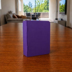 Puede incluir: Un estuche de almacenamiento rectangular de color morado s&oacute;lido con un acabado mate suave y un panel lateral con bisagras. El objeto se mantiene en posici&oacute;n vertical sobre su base, con un dise&ntilde;o limpio sin patrones, texto ni herrajes visibles.