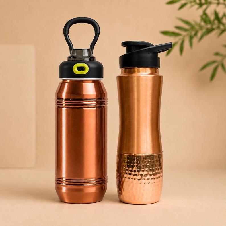 Op de afbeelding: Twee koperkleurige metalen waterflessen. De linkerfles heeft een zwarte dop met een limoengroene knop en een ronde handgreep. De rechterfles heeft een zwarte klapdeksel en een gehamerde textuur op de onderste helft van de behuizing.