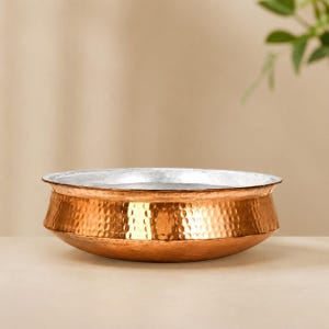 May include: A wide, shallow bowl featuring a hammered copper exterior with a warm, metallic finish and a smooth, silver-toned interior. The vessel has a distinct, angled rim that transitions from the textured copper base to the polished metal edge.