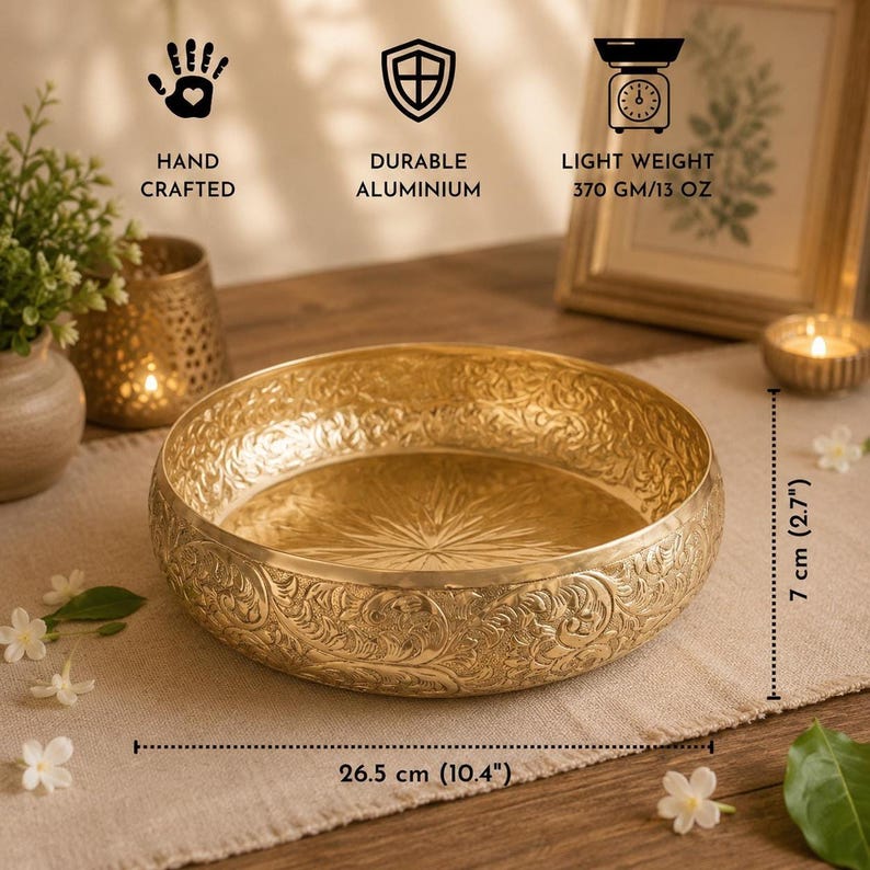 An empty gold metal urli bowl with embossed exterior detailing and an engraved starburst pattern on the inside base, showing product dimensions of 26.5 cm by 7 cm and feature icons.