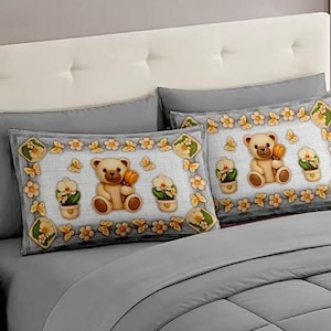 May include: Two gray pillowcases with a decorative border featuring a teddy bear holding a honey pot, flowers, and butterflies. The pillowcases are on a gray bed with a white headboard.