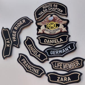 Peut inclure: Un ensemble d'écussons brodés noirs avec des lettres dorées et blanches. Les écussons présentent des textes tels que Route 66 Tulsa Chapter, Free Rider, Kai, Angela, Francine, Daniela, Germany, Life Member, Zara et un emblème d'aigle Harley Owners Group.