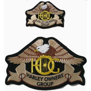 May include: Two embroidered patches featuring a bald eagle with spread wings above a yellow HOG logo and a tan banner with the text HARLEY OWNERS GROUP. The patches have a black background and are shaped with a pointed top and curved bottom edges.