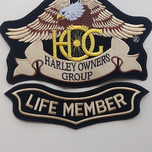 Puede incluir: Dos parches bordados con fondo negro. El parche superior muestra un águila calva con las alas extendidas sobre un logotipo HOG amarillo y una cinta con el texto HARLEY OWNERS GROUP. El parche inferior es una cinta curva con el texto LIFE MEMBER.