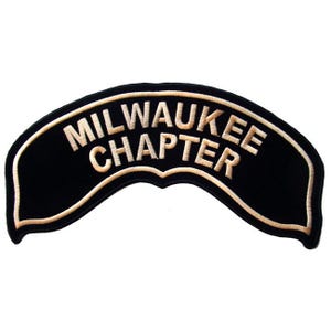 Peut inclure: Un écusson brodé noir en forme d'arc portant le texte MILWAUKEE CHAPTER en lettres capitales épaisses de couleur claire. L'écusson présente une bordure épaisse de couleur claire qui suit la forme arquée du motif, créant un contour distinct.