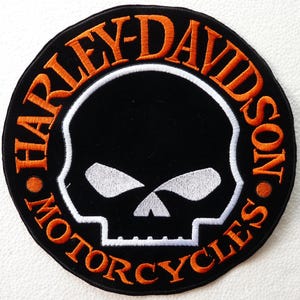 Puede incluir: Un parche bordado circular con fondo negro y borde naranja. El texto HARLEY-DAVIDSON MOTORCYCLES está bordado en naranja alrededor del perímetro. Un gráfico de calavera blanca está centrado dentro de un contorno circular blanco.