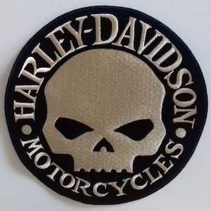 Puede incluir: Un parche bordado circular que presenta una calavera de color tostado centrada sobre un fondo negro. El texto HARLEY-DAVIDSON MOTORCYCLES está bordado con hilo tostado en un borde circular alrededor de la calavera, separado por dos puntos.