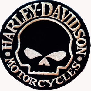 Könnte beinhalten: Ein kreisförmiger, schwarz bestickter Aufnäher mit dem weißen Schriftzug Harley-Davidson Motorcycles, der ringförmig um eine stilisierte weiße Totenkopf-Grafik angeordnet ist. Das Design ist mit einem dicken weißen Rand auf schwarzem Stoff.