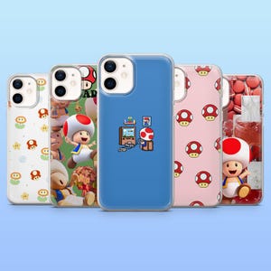 Könnte beinhalten: Eine Sammlung klarer Handyhüllen mit verschiedenen Designs. Eine Hülle hat einen blauen Hintergrund mit einem pixeligen Bild eines Charakters, der ein Videospiel spielt. Andere Hüllen zeigen Pilz- und Charaktergrafiken auf weißem und rosa Hintergrund.