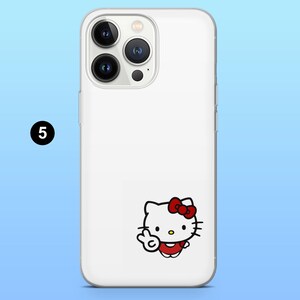 May include: White phone case featuring a Hello Kitty graphic. The cartoon character is wearing a red dress and bow, and is giving a peace sign. The phone case has a clear border and a camera cutout.