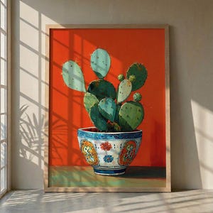 May include: A framed art print showing a cactus in a decorative pot. The cactus has green and blue-green pads and sits in a blue and white patterned pot. The background is a vibrant orange, and the frame is a light wood colour.