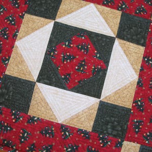 May include: A festive Christmas-themed quilted table runner. The design features a central square with a red fabric adorned with Christmas trees, surrounded by white, black, and tan geometric shapes. The border is red with Christmas tree patterns.