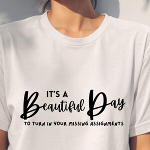May include: White t-shirt with the text "It's a Beautiful Day to turn in your missing assignments" in black script. The shirt is a crew neck style and is being worn by a person.