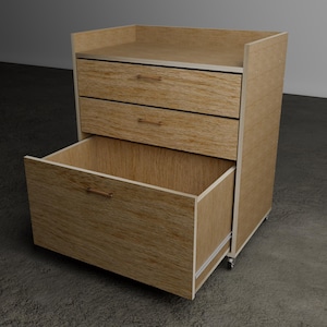 Puede incluir: Un mueble de almacenamiento de madera de color marrón claro con dos cajones superiores y un cajón inferior grande y profundo que está totalmente extendido. Tiene una superficie superior plana con un pequeño borde trasero y ruedas.