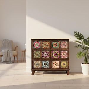Puede incluir: Un mueble de madera marrón oscuro con nueve cajones, cada uno con un diseño colorido y estampado. Los patrones incluyen motivos florales y geométricos en varios colores. El mueble está colocado contra una pared blanca con una planta en maceta blanca.