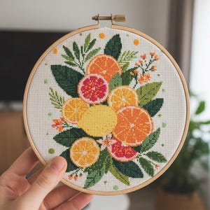 May include: A cross-stitch embroidery hoop featuring a vibrant citrus fruit design. The artwork showcases oranges, lemons, and grapefruits, with green leaves and small orange flowers. The embroidery is set in a wooden hoop.