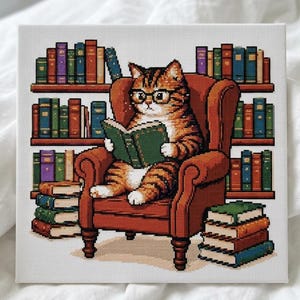 May include: A square cross-stitch embroidery piece featuring a ginger tabby cat wearing black-rimmed glasses, sitting in a brown armchair while reading a green book. The cat is surrounded by multiple shelves filled with colorful books.