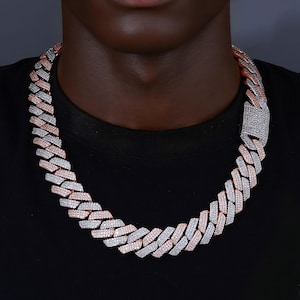 Puede incluir: Un collar de cadena de dos tonos con acabado en oro rosa y plata. El collar está hecho de eslabones entrelazados y tiene un cierre rectangular. La joya se lleva alrededor del cuello y está sobre un fondo negro.