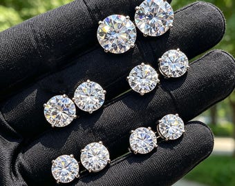 May include: A collection of round, brilliant-cut clear stones set in silver-toned metal prongs. These stud earrings feature faceted surfaces that reflect light, arranged in pairs across a black fabric-covered surface to display their clarity.