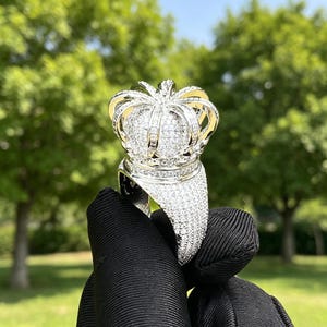 May include: A silver-toned ring shaped like a crown, featuring a high-polish metal finish and an intricate surface entirely encrusted with numerous small, clear, sparkling stones that cover the band and the arched top structure.