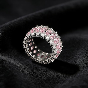 Peut inclure: Une bague en argent ornée de rangées alternées de pierres roses et transparentes. La bague est présentée sur un fond noir, mettant en valeur l'éclat des pierres. C'est une bague de type alliance.