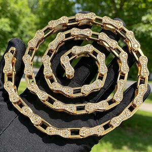 Peut inclure: Un collier à chaîne doré composé d'une série de maillons interconnectés en forme de segments de chaîne de vélo. Chaque maillon individuel est incrusté de nombreuses petites pierres claires et scintillantes recouvrant toute la surface.