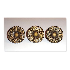 May include: Three antique brass-colored cabinet knobs. Each knob features a central sphere surrounded by an ornate, floral-inspired design. The knobs are circular and have a vintage aesthetic.
