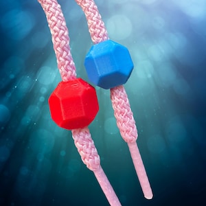 Peut inclure: Gros plan sur deux lacets roses avec des perles géométriques rouges et bleues. Les lacets sont tressés et de couleur rose clair. Les perles sont à facettes multiples et ont une texture lisse. Le fond est un dégradé de bleu et de turquoise.