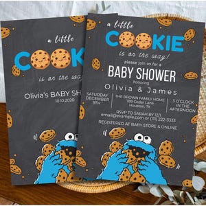 May include: Two baby shower invitations with a chalkboard design. The invitations feature the text "a little COOKIE is on the way!" with cookie illustrations and the names Olivia & James. The invitations are decorated with cookie illustrations.