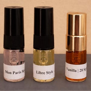 Puede incluir: Tres pequeños frascos de perfume con tapas negras y doradas. Los frascos tienen etiquetas blancas con los textos "Mon Paris Style", "Libre Style" y "Vanilla | 28 S". Los líquidos del interior son rosas, amarillos y marrones.