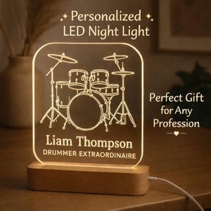 May include: A personalised LED night light featuring a drum kit design. The light is engraved with the name "Liam Thompson" and the text "DRUMMER EXTRAORDINAIRE". It sits on a wooden base and is plugged in.