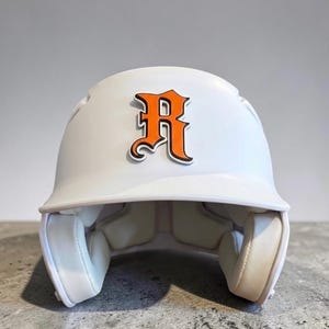 May include: A matte white baseball batting helmet featuring a prominent orange letter R with a black outline centered on the front. The interior of the helmet is lined with white protective padding, and the exterior has a smooth, solid finish.
