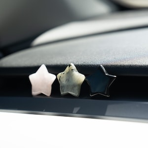 May include: Three star-shaped carvings arranged in a row. The first is a pale pink stone, the second is a speckled grey and white stone with dark inclusions, and the third is a solid, smooth, glossy black stone. Each piece has five points.