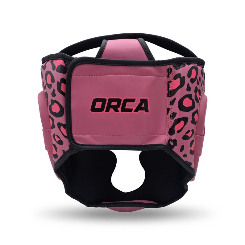 May include: A pink head guard with black trim and the word "ORCA" in pink. The sides feature a leopard print pattern in pink and black. The headgear is designed to protect the head during sports activities.