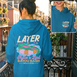 Peut inclure: Sweat à capuche bleu sarcelle avec le mot "LATER" en police vintage au dos. En dessous, un dessin d'un alligator sur une bouée rose et orange. Le texte "Kylie's Last Bayou Bash - NOLA 2026" est en dessous. Une version plus petite du dessin est sur le devant.