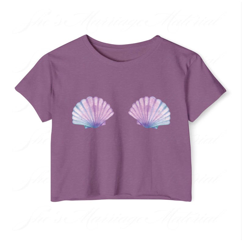 May include: A purple crop top with two seashell designs in blue, pink, and purple. The seashells are positioned centrally on the front. The top has short sleeves and a round neckline.