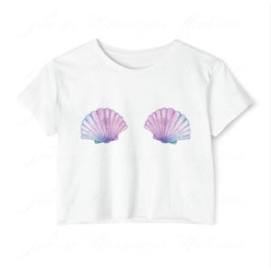 May include: White t-shirt with a watercolour design of two seashells. The shells are in shades of purple, blue, and pink. The shirt has a classic crew neck and short sleeves. The design is centered on the chest.