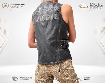 May include: A black leather vest featuring the text Harley-Davidson embroidered in a metallic silver font across the upper back. The vest includes two adjustable side buckles with metal hardware and a vertical zipper closure at the lower back hem.