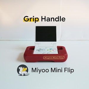 May include: A handheld gaming device with a burgundy red base and a white screen. The device has a white control panel with gray buttons and colorful accent buttons. The text "Grip Handle" and "Miyoo Mini Flip" are visible.