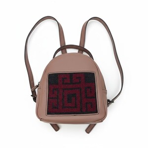 Könnte beinhalten: Ein kleiner, staubrosa Rucksack mit verstellbaren Trägern. Die Vorderseite hat ein rechteckiges Feld mit einem geometrischen Design in Schwarz und Burgunderrot. Der Rucksack hat einen oberen Griff und ist aus glattem Material gefertigt.