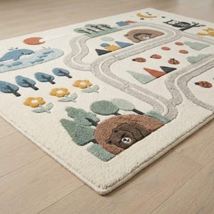 Puede incluir: Una alfombra de color crema con un dise&ntilde;o de relieve sobre la naturaleza que incluye un camino gris sinuoso, una ballena azul, flores amarillas, &aacute;rboles verdes, osos pardos en sus guaridas, mariquitas, un b&uacute;ho, una luna creciente y un sol.