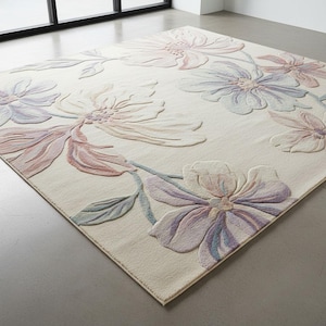 Puede incluir: Una alfombra rectangular con un fondo de color crema y grandes motivos florales en relieve en tonos pastel suaves de rosa, lavanda y azul claro. Las flores presentan una apariencia texturizada y esculpida con pétalos y hojas visibles.