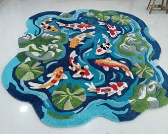 以下が含まれることがあります： オレンジ、白、赤、黒の鯉が複数描かれた池の風景の不規則な形のラグ。緑の睡蓮の葉と灰色の岩の形が、渦巻く青い水の背景に配置されています。鯉の模様は鮮やかで、池の水の流れを表現した青い曲線が全体に広がっています。