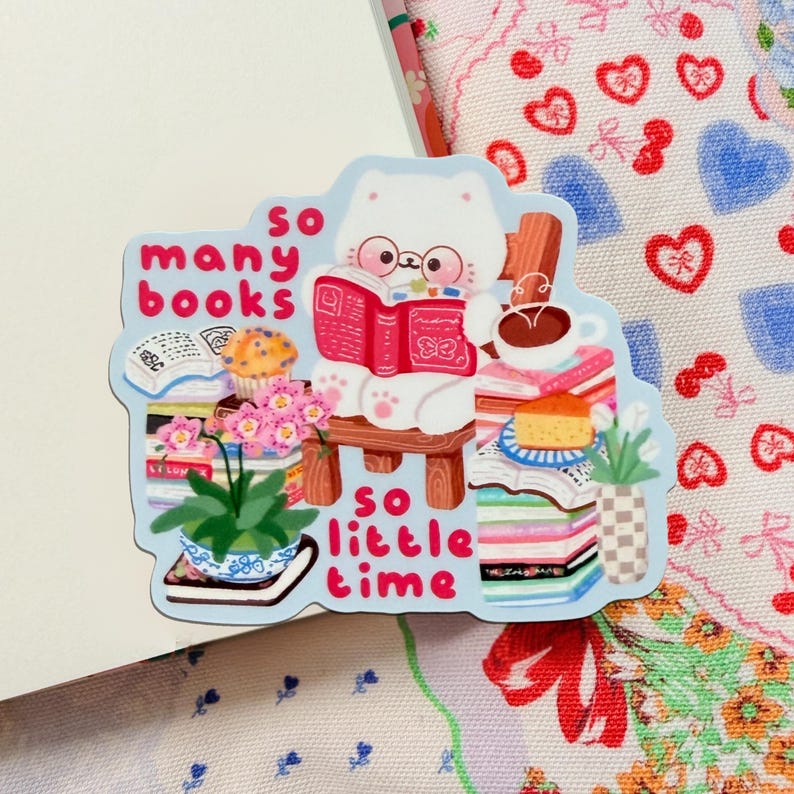 May include: A sticker depicting a white cat reading a red book, with the words "so many books, so little time." The cat is on a wooden chair, surrounded by books, a coffee cup, and plants. The sticker has a light blue border, and is a cute illustration.