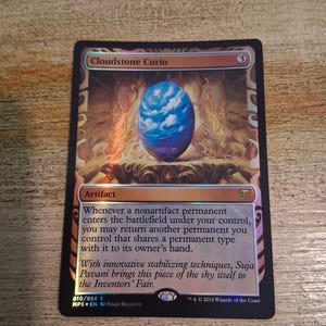 May include: A Cloudstone Curio card featuring a blue and white orb with a cloudy sky design. The card has text that reads "Cloudstone Curio" and "Artifact". The card is set against a background of gold and orange hues.