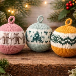 May include: Three knitted Christmas ornaments in pink, light blue, and yellow, each with a loop for hanging. The pink ornament features a pattern of brown figures holding hands. The light blue ornament has a green Christmas tree design, and the yellow one has a green zigzag pattern.