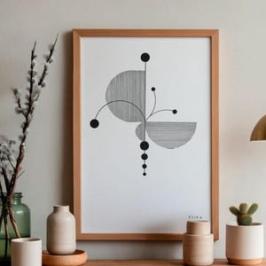 Könnte beinhalten: Gerahmter Kunstdruck mit einem abstrakten geometrischen Design in Schwarz und Weiß. Das Kunstwerk wird auf einer Holzoberfläche zusammen mit dekorativen Vasen, einem Kaktus und einer hängenden goldfarbenen Lampe präsentiert.