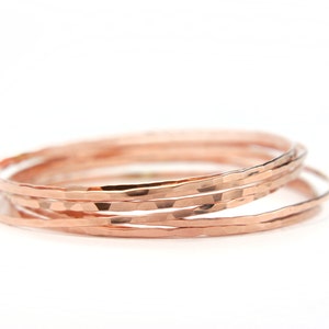 May include: Set of six rose gold hammered metal bangles. The bangles are stacked on top of each other.