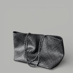 May include: A black tote bag with a woven design. The bag has two braided handles and a rectangular shape. The material appears to be leather or a leather-like material. The bag is set against a gray background.